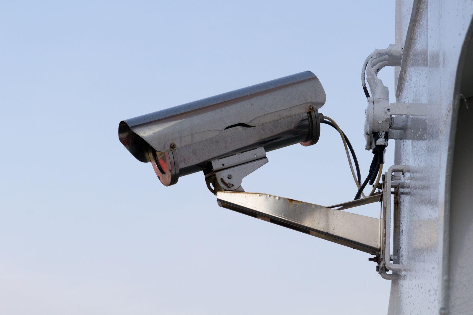 An outdoor security camera mounted on a wall against a pale sky