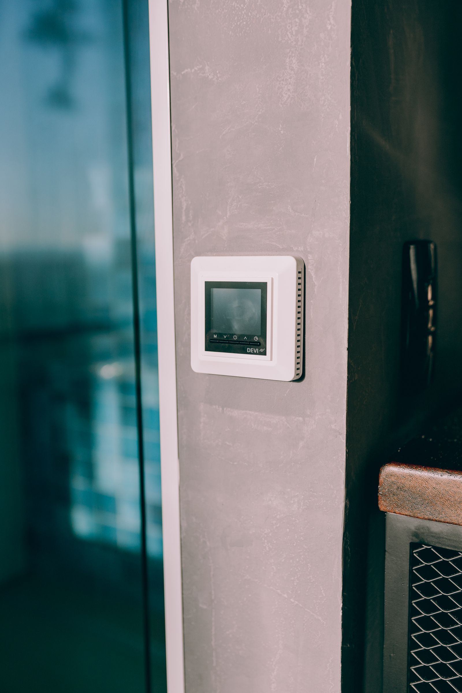 A digital thermostat mounted on a wall next to a window