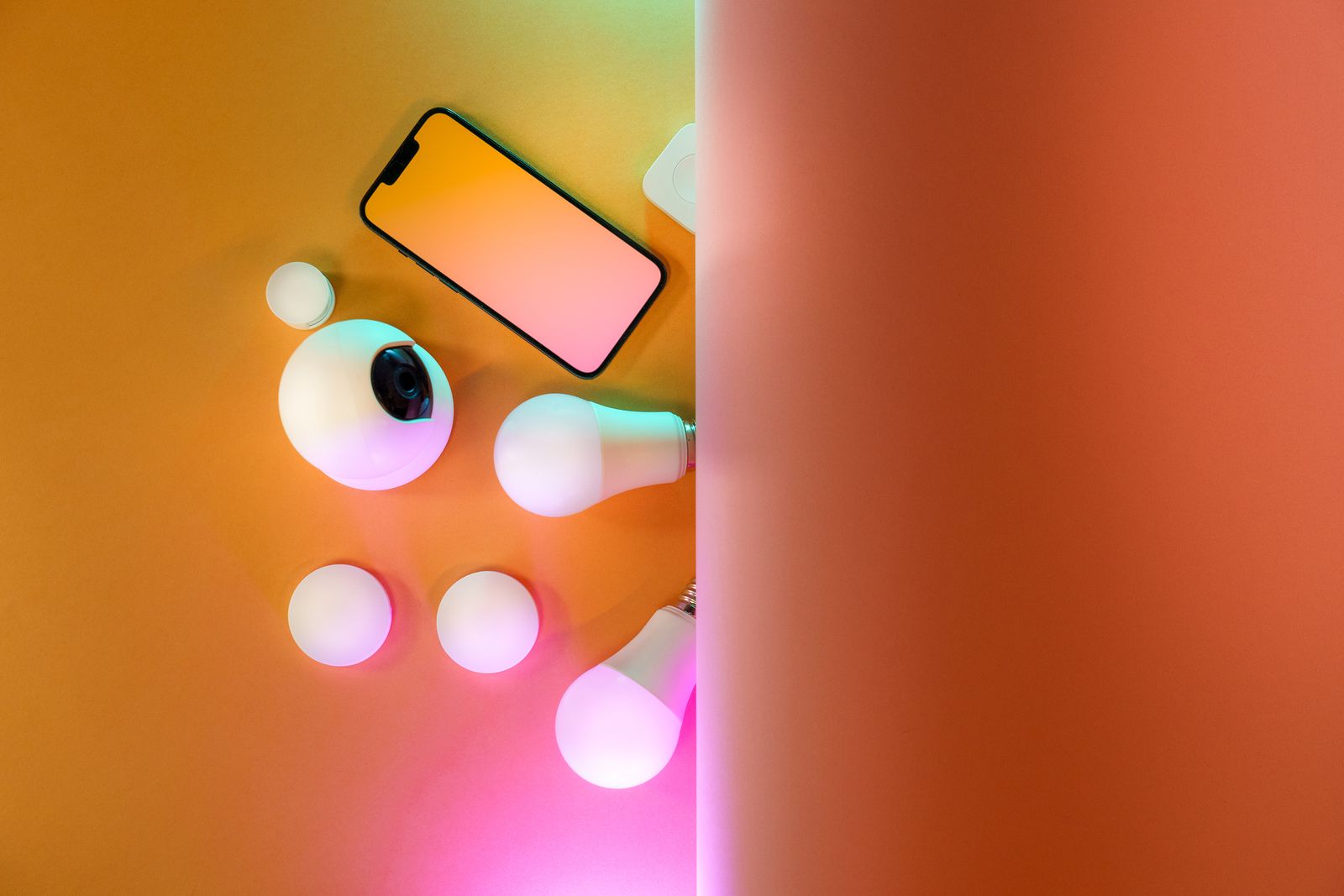 Flat lay of smart bulbs, a camera and a phone on a colourful background