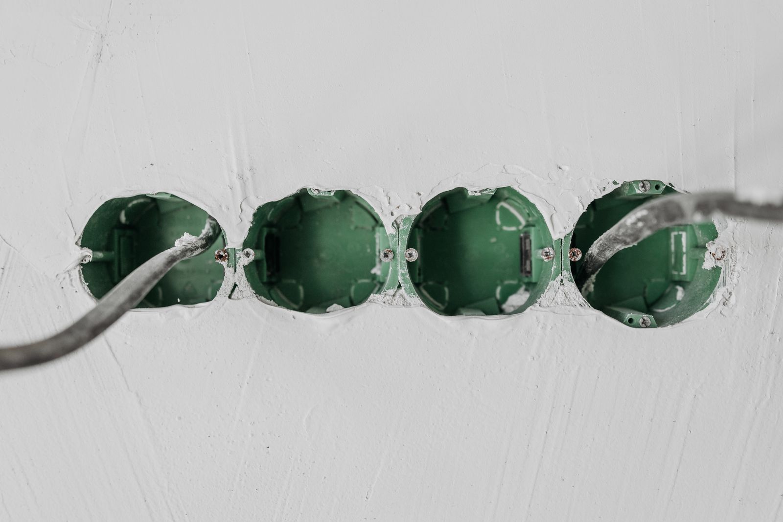 Four empty green flush-mounted wall boxes in a white wall with cables coming out